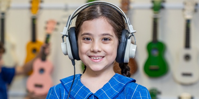 student wearing headphones in a music learning space with instruments in the background, highlighting engagement in music education and creative development