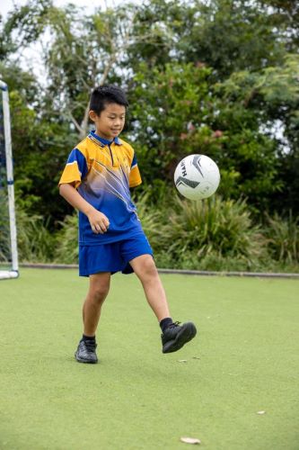 student practising ball control during outdoor play on a school field, highlighting active participation, coordination and physical development