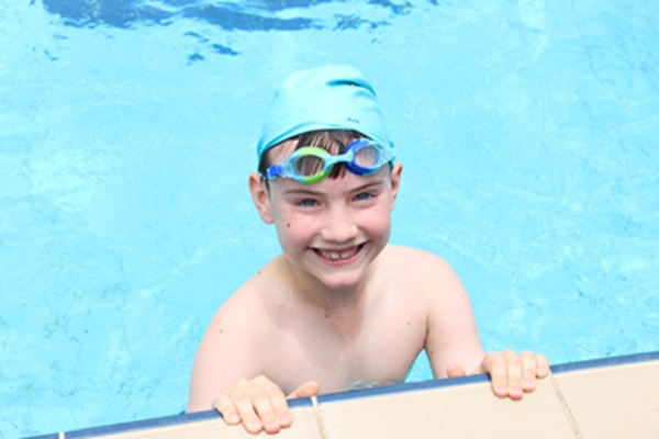 student smiling at the pool wearing swim cap and goggles, representing participation in swimming, confidence and physical activity
